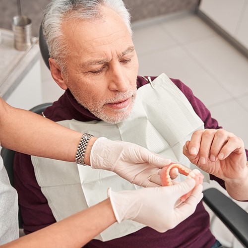 A dentist showing dentures to their older male patient