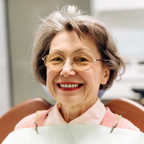 An older woman smiling while sitting in a dentist’s chair
