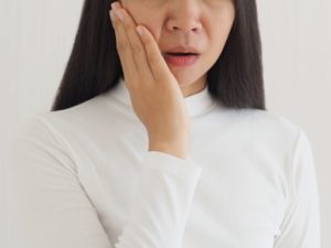 Woman in white turtleneck holding her hand to her jaw in pain